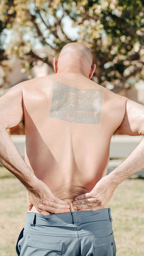 bald man with tattoo holding lower back, back view