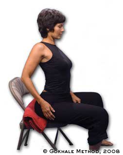 Esther Gokhale sitting on a chair while demonstrating her previous habit of arching the back to be "upright".