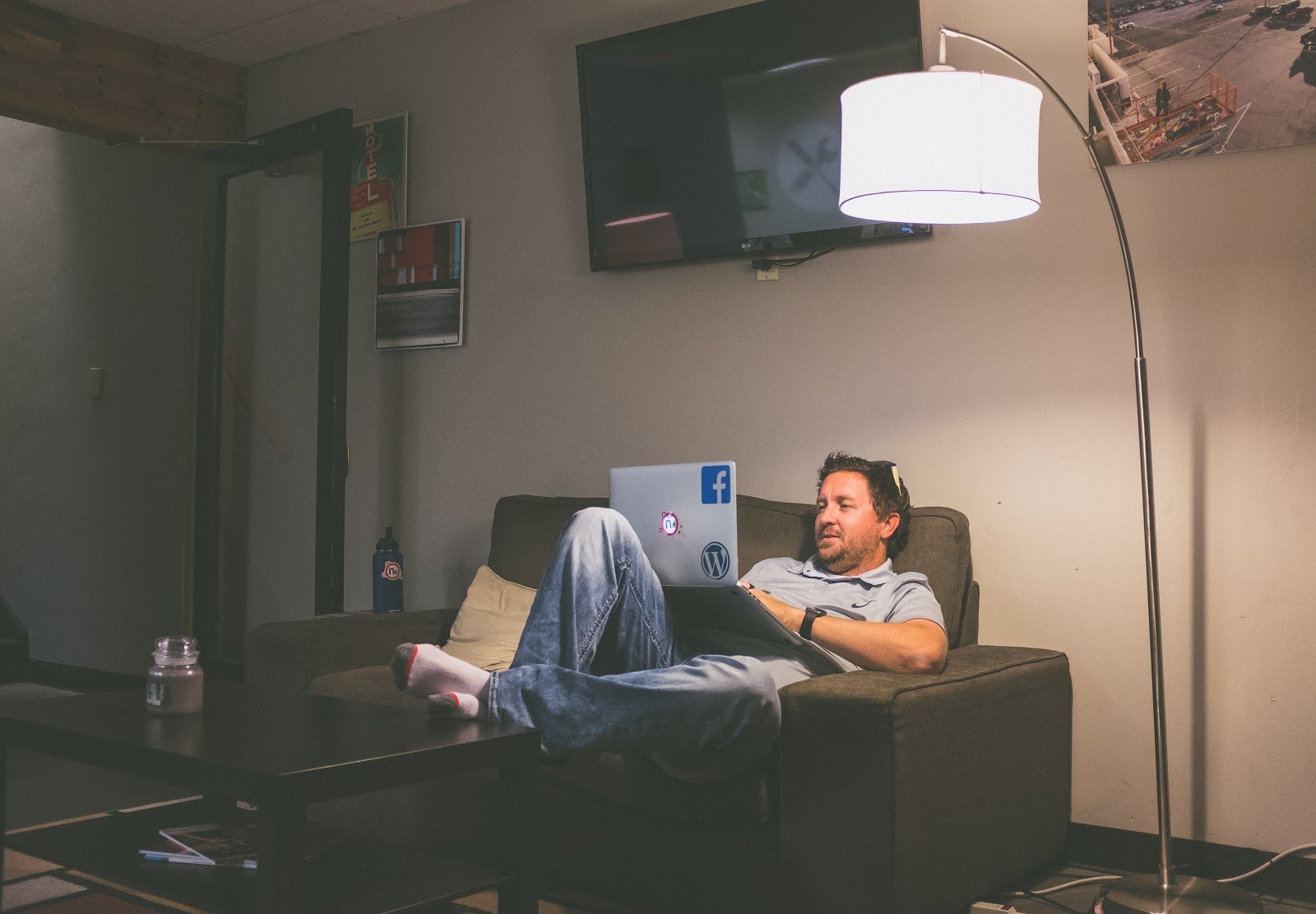 Man very slumped on sofa, laptop, overhanging lamp