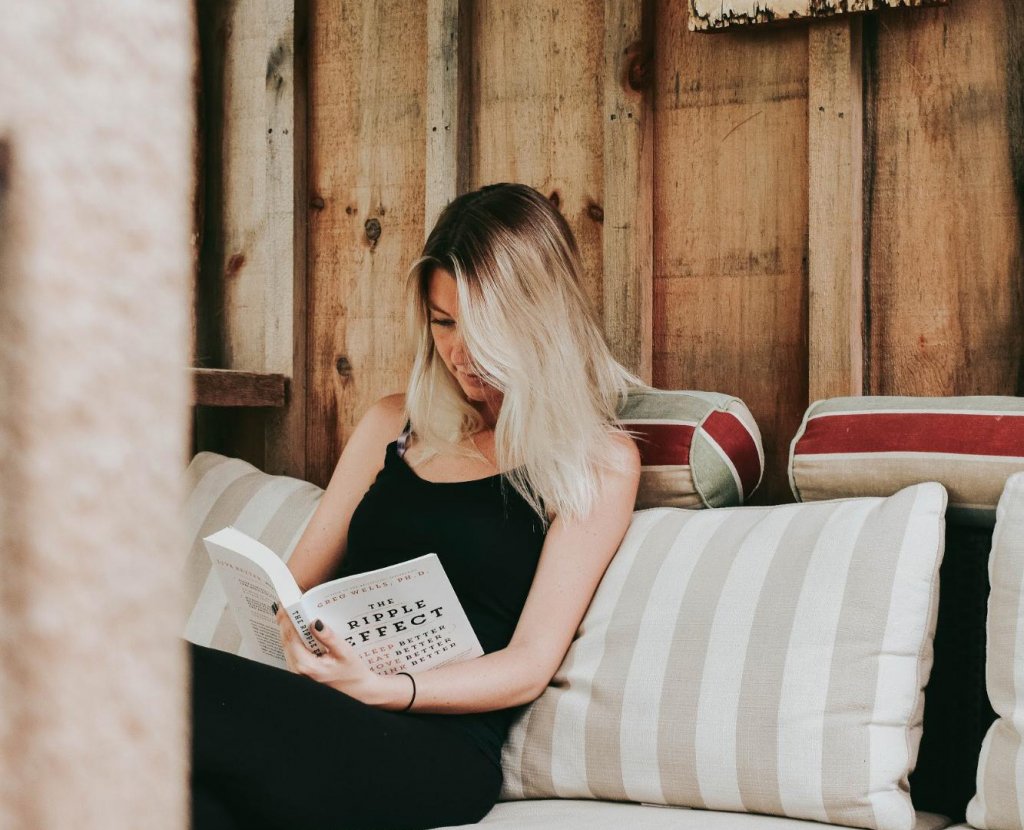 Woman on sofa reading book with cushions supporting