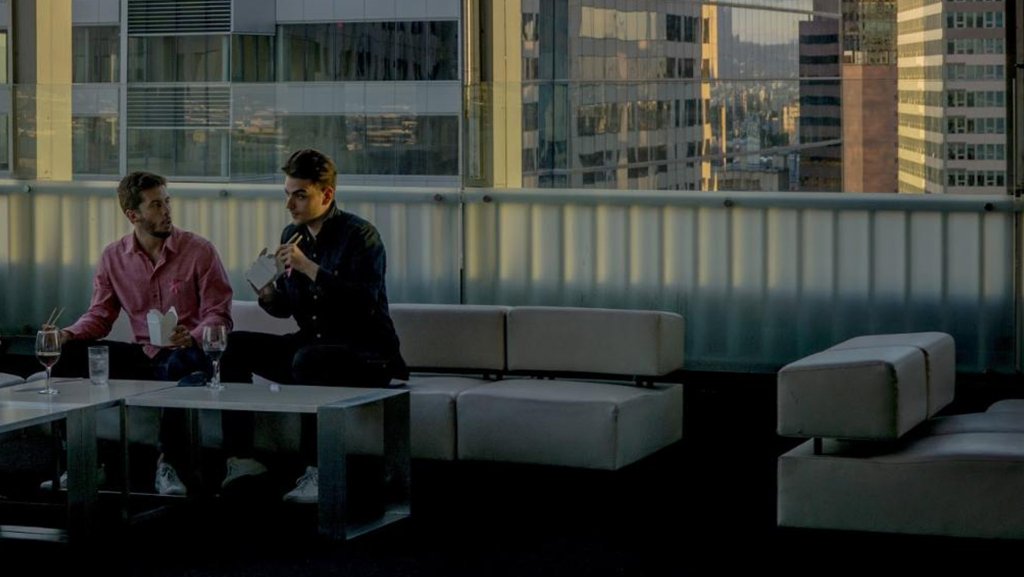 Two men sitting upright on sofa edge.