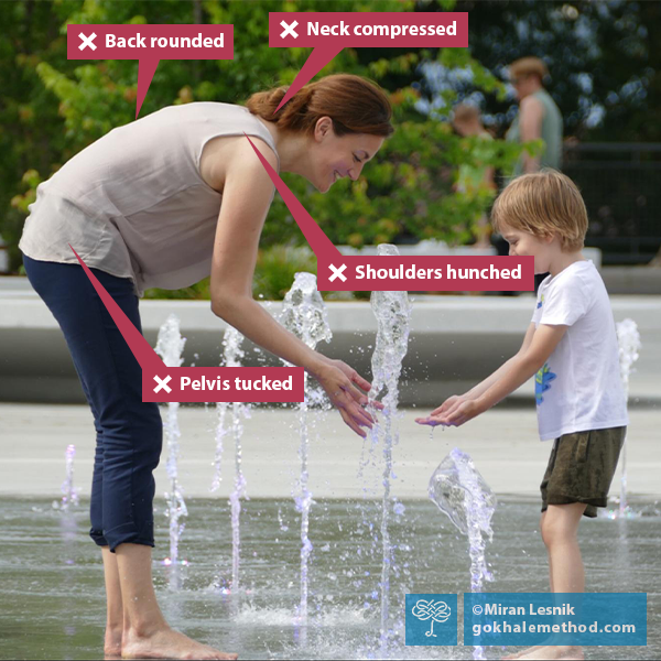 Photo of woman round back bending with young boy, playing with water feature.