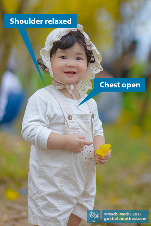 Child in white bonnet smiling and picking flowers with beautiful upright posture