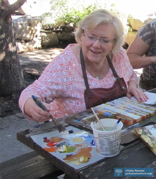 Gokhale Method Alumna Kathy Nauman sitting painting at art class.