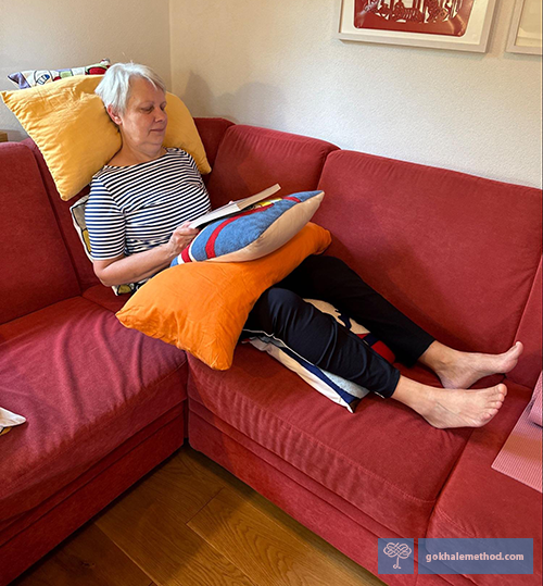 Gokhale Method student Heika Eschbach stretch-reclining reading on the sofa.