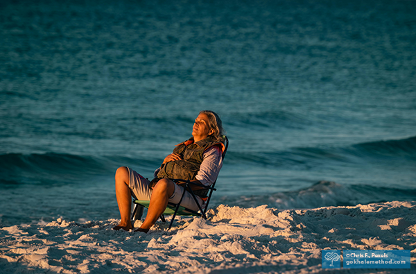 Photo of a woman reclining in a beach chair by the sea, evening light.