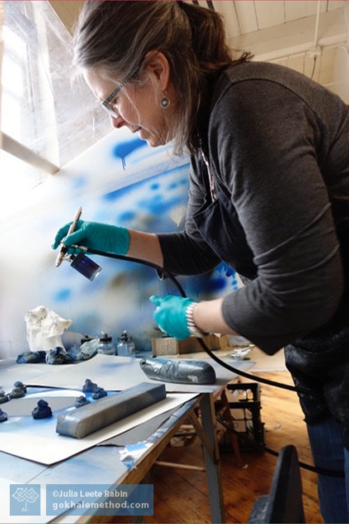 Julia Rabin hunching painting a book cover.