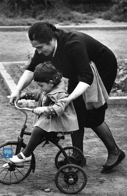 Young girl on large tricycle, guided by bending over woman, Ken Hyman, Pinterest