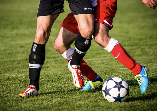 Two soccer players tackle for the ball, showing lower limbs only.