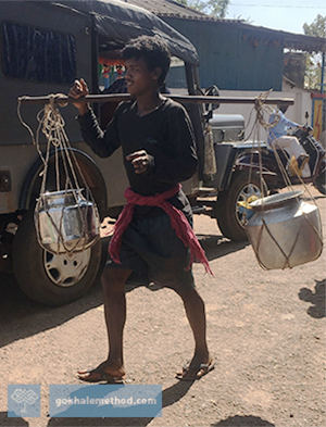 Man in India walking carrying pitchers on yoke. 