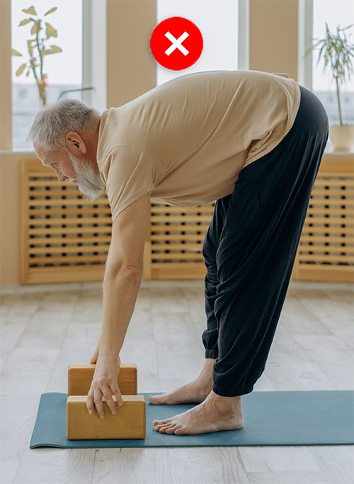 Yoga model in standing forward bend, side view, touching blocks, rounded back.
