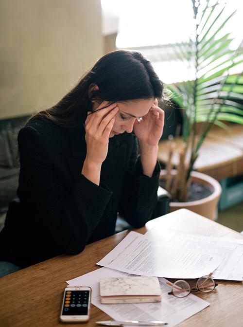 Woman at desk with headache, head in hands.